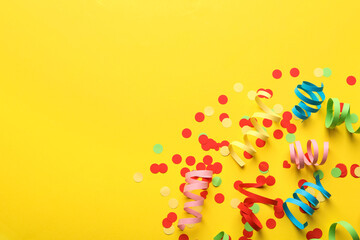 Colorful serpentine streamers and confetti on yellow background, flat lay. Space for text