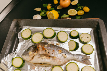 Big fish is being prepared for the oven. Fish on aluminum foil on a black plate. Healthy food with...