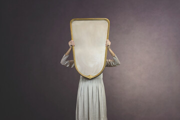 woman hides holding a mirror in front of her face; introspection concept