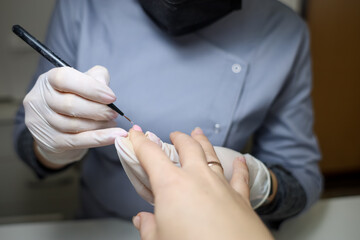 client is undergoing a procedure with a manicure master. Manicurist apply gel polish to nails