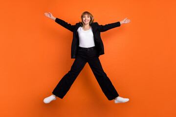 Fototapeta na wymiar Full size photo of young happy excited good mood girl jumping with open hands wear black suit isolated on orange color background