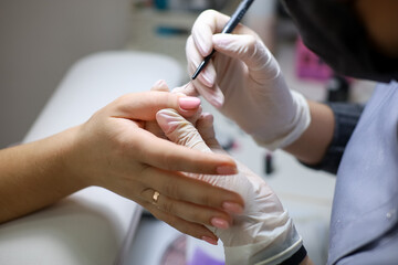 manicurist makes the client a manicure by applying nail polish. A manicure master in white gloves works with the client's nails