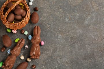 Flat lay composition with chocolate Easter bunnies, eggs and candies on grey table. Space for text