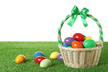 Wicker basket with Easter eggs on green grass against white background. Space for text