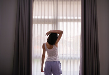 Fototapeta na wymiar Young Asian woman stretching in bed after wake up, back view