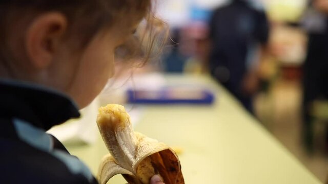 kindergarten little girl eating a banana for lunch at playtime