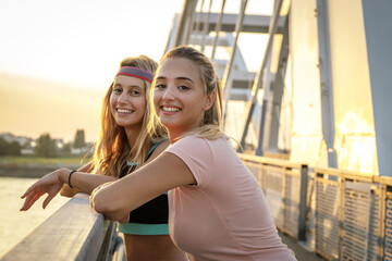 Two best friends relaxing after jogging over the city bridge.Joying in sunset.