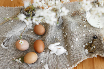 Fototapeta na wymiar Natural Easter eggs, bunnies, feathers, nest and cherry blooming branch with petals on rustic linen