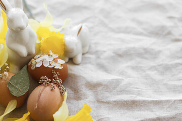 Stylish Easter eggs decorated with dry flowers on rustic linen napkin with daffodils and bunnies