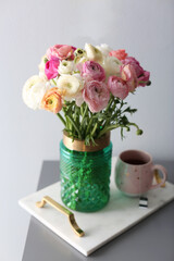 Bouquet of beautiful ranunculuses and tea on table near light grey wall