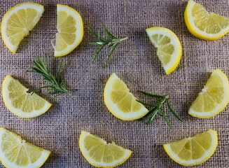 Flat lay half slices of lemon with rosemary twigs on natural hessian background