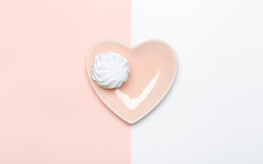 White marshmallow on a pink plate in the shape of a heart on a pink and white background