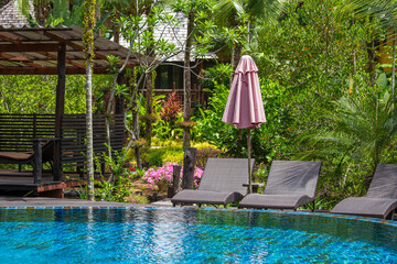 Swimming pool with relaxing beds and sun umbrella in tropical garden