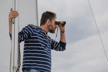 Man is sailing  yacht and looking through binoculars