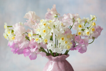 Bouquet in a vase of sweet pea flowers and daffodils on a decorative colored background. Close-up, blur, selective focus.