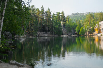 Fototapeta premium The green forest is reflected in the water. Rock on the lake shore. Summer landscape