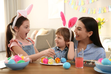 Happy mother with her children painting Easter eggs at table indoors