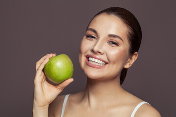 Lovely woman holding green apple and smiling on brown background