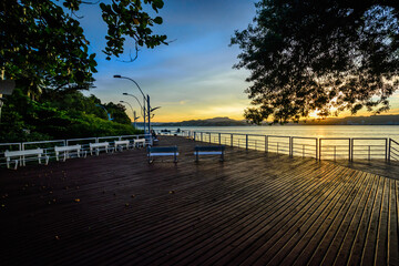 Public wooden deck by the sea at sunset, calm sea and hills on the horizon