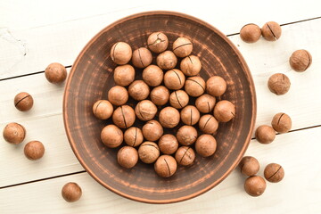 Several ripe brown macadamia nuts on a clay plate, close-up, on a wooden table.