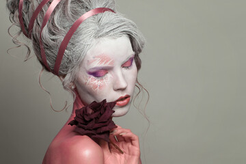 Nice woman with creative makeup and hairstyle holding dried rose flowers on gray background