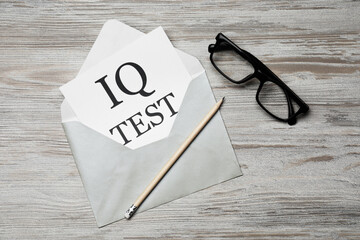 Paper with words IQ Test in envelope, pencil and glasses on wooden table, flat lay