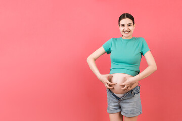 pregnant woman dressed in opened jeans scratching her belly at colorful background with copy space. Problem of stretch marks concept