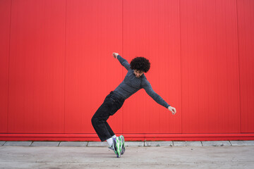 Chico joven bailando y sonriendo delante de una pared roja
