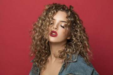 Attractive young woman with curly hair on red background