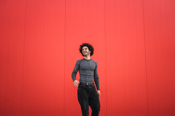 Chico joven bailando y sonriendo delante de una pared roja