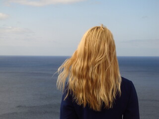 Dziewczyna z blond włosami patrze daleko w horyzont nad morzem - obrazy, fototapety, plakaty
