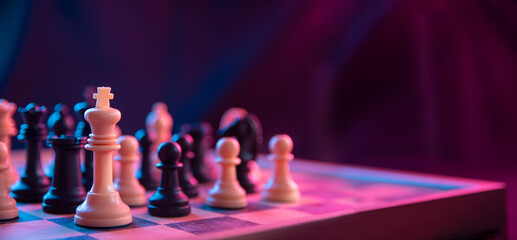 Chess pieces on a chessboard on a dark background shot in neon pink-blue colors. The figure of a chess .Close up. - obrazy, fototapety, plakaty
