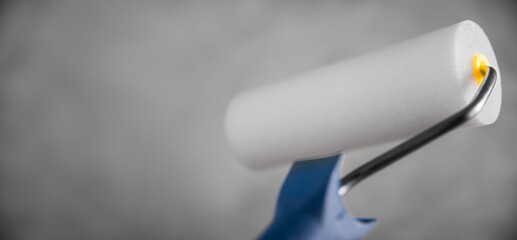 Clean fresh new paint roller for painting on gray blurred concrete background. Close up with copy empty space for text. Banner for advertising.