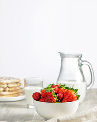 Health food. White plate with fresh strawberries, glass with milk, milk jug and waffles. High key. Close up. Selective focus. Vertical orientation.