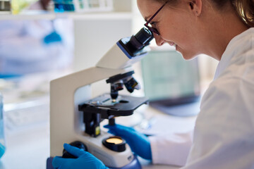 Smiling female lab technician looking at samples under a microscope