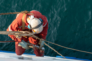Seaman ship crew working aloft at height derusting and getting vessel ready for painting.
