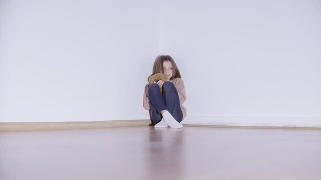 Frightened child sitting in the corner, hugging teddy bear toy, punishment