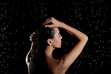 Young woman washing hair while taking shower on black background