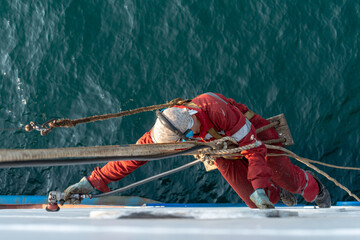 Seaman ship crew working aloft at height derusting and getting vessel ready for painting.