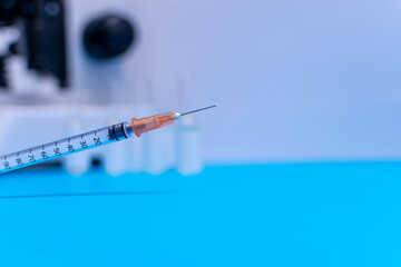 The syringe in the foreground with blurred background of microscope and vaccine bottles. The concept of injection, vaccine, care, treatment, human and animal research.
