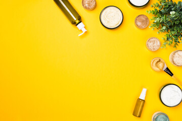 Cosmetic containers with skincare products on illuminating yellow background. Natural body scrub and moisturizing face cream or skin clay mask. Flat lay composition, copy space