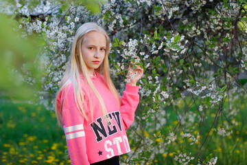 Pretty teen girl are posing in garden near blossom tree with white flowers. Spring time.