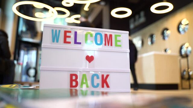 A lightbox with the inscription WELCOME BACK. We are open again after the quarantine, a photo of a small business owner.