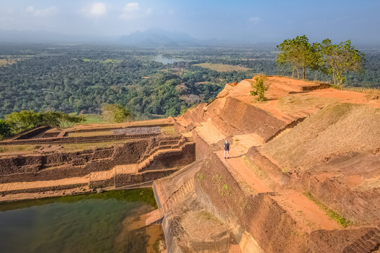 A lone blonde caucasian female backpacker tourist visits the terraced gardens  atop the ancient historic Sigiriya Rock Fortress or Lion Rock in Sri Lanka.