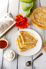 Pancakes with jam and sour cream, breakfast, orange flower, spring, woman's day. Traditional russian blini on white wooden table. Pancake week. Shrovetide. Regional food. Close up. Vertical format.