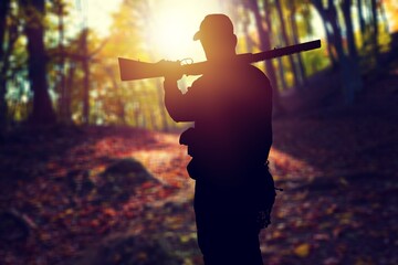 Male hunter silhouette with a gun at sunset
