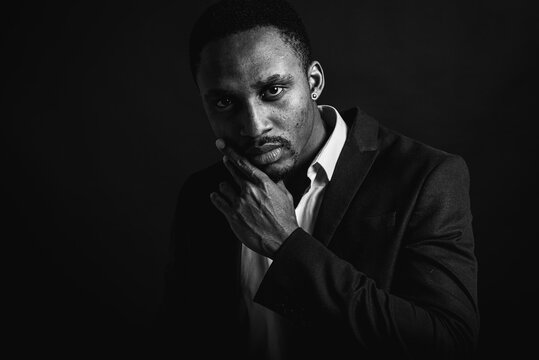 Portrait of attractive, handsome, stylish professional African American businessman in stylish suit and white shirt pensive holding hand near face, isolated on dark background. Low key. Selective focu