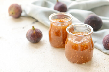 Glass jars with sweet fig jam on light background