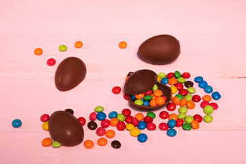Chocolate Easter eggs with colored sweets on wooden background.