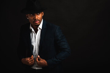 Portrait of attractive, cute, stylish professional African American businessman in stylish suit, white shirt and black hat, isolated on dark background. Low key. Selective focus